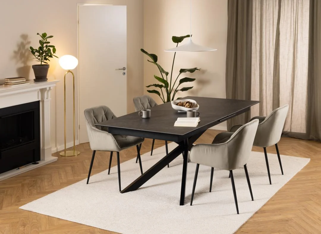 Een moderne eetkamer met de Eettafel Nieuwe Sfeer 100 x 76 CM Rechthoek Keramiek, vier beige gestoffeerde stoelen, een wit vloerkleed, potplanten, een staande lamp, een broodschaal en transparante gordijnen die natuurlijk licht binnenlaten.