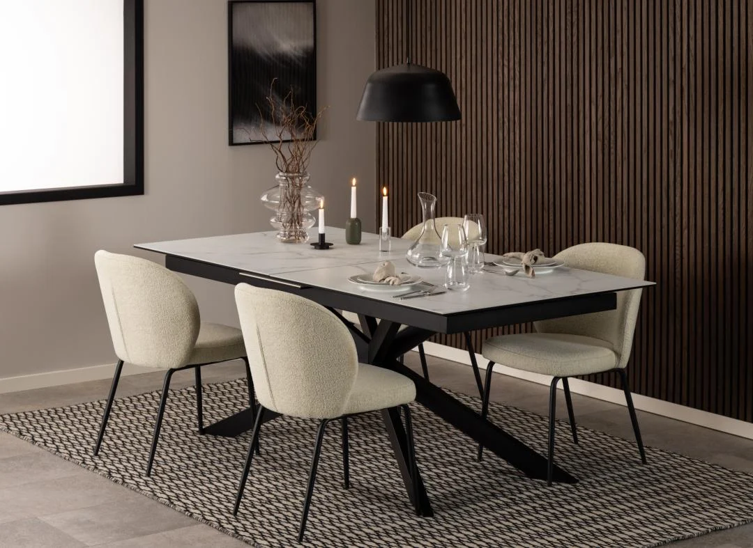 Een moderne eetkamer met de Eettafel Irwine 240 x 100 CM Rechthoek keramiek tafel, vier crèmekleurige stoelen, kaarsen, glaswerk, minimalistische inrichting, een zwarte hanglamp erboven en een accentmuur van structuurhout op de achtergrond.