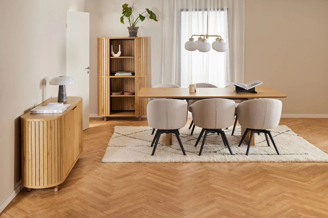 Een moderne eetkamer met de Eettafel Nieuwe Sfeer 100 x 75 CM (rechthoek MDF), zes beige stoelen, een dressoir, hoge kast, wit vloerkleed op houten vloer, groot raam met transparante gordijnen en minimalistisch decor met planten en lampen.