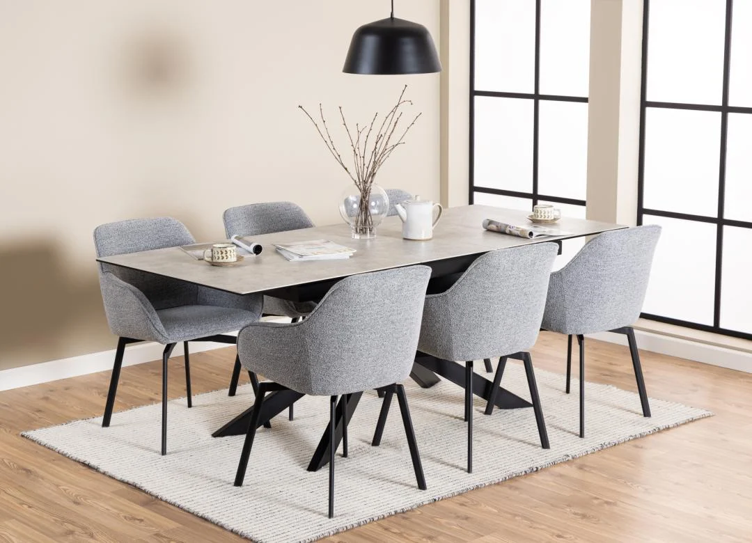 Moderne eetkamer met de Eettafel Irwine 90 x 76 CM rechthoekige tafel in keramiek staal, zes grijze stoelen met kussens, een zwarte hanglamp en decor waaronder een theepot, kopjes en een vaas met takken op een licht vloerkleed op een houten vloer.