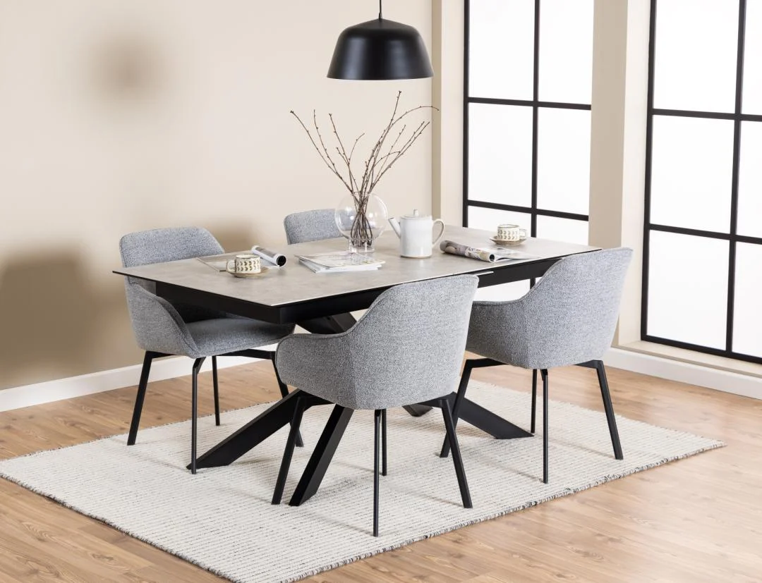 Een moderne eethoek met de Eettafel Irwine 90 x 76 CM Rechthoek in keramiek staal, vier grijze stoelen met kussens, een zwarte hanglamp, witte theepot en kopjes, minimalistische inrichting, grote ramen, lichte houten vloeren en een wit vloerkleed.