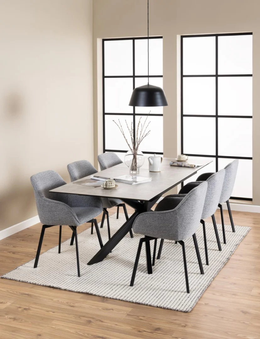 Een moderne eetkamer met de Eettafel Irwine 90 x 76 CM Rechthoek keramiek staal tafel, zes grijs gestoffeerde stoelen, een zwarte hanglamp, minimalistische inrichting, grote rasterramen en een wit vloerkleed met structuur op een houten vloer.