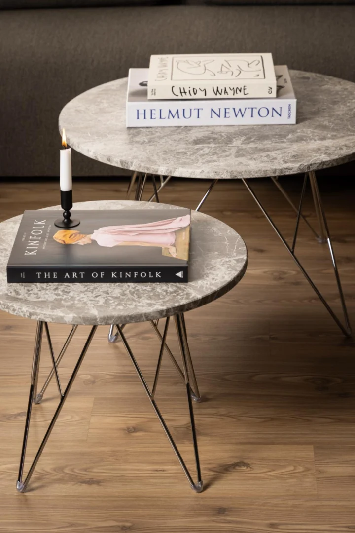 A Salontafel Grijs, Bruin 80 CM Rond van kunststof staat op een houten vloer. Op tafel liggen de boeken "Chidy Wayne" en "Helmut Newton", en er staat een kaars naast "The Art of Kinfolk".