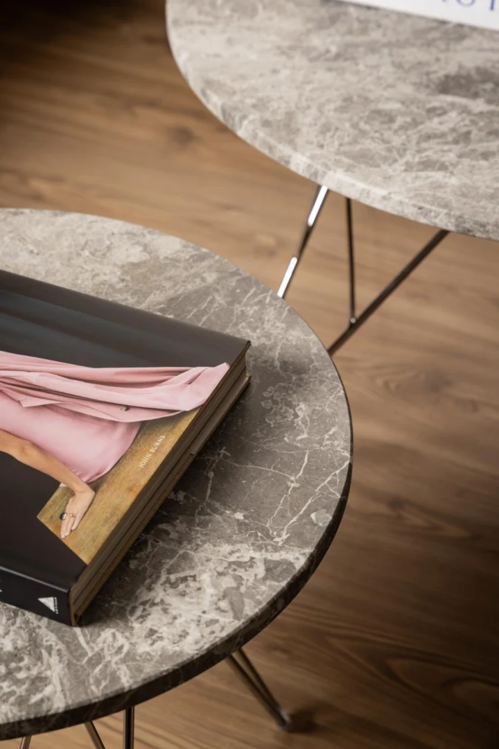 Een tijdschrift met een persoon in een roze outfit ligt op Salontafel Grijs, Bruin 80 CM Rond, een ronde grijze plastic tafel, naast een soortgelijke tafel op een houten vloer.