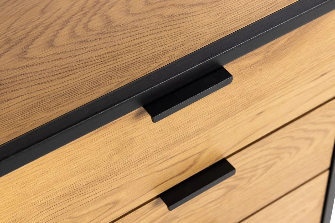 Detailopname van een ladekast in eikenlook met zwarte metalen handgrepen, warme belichting en een strak design.