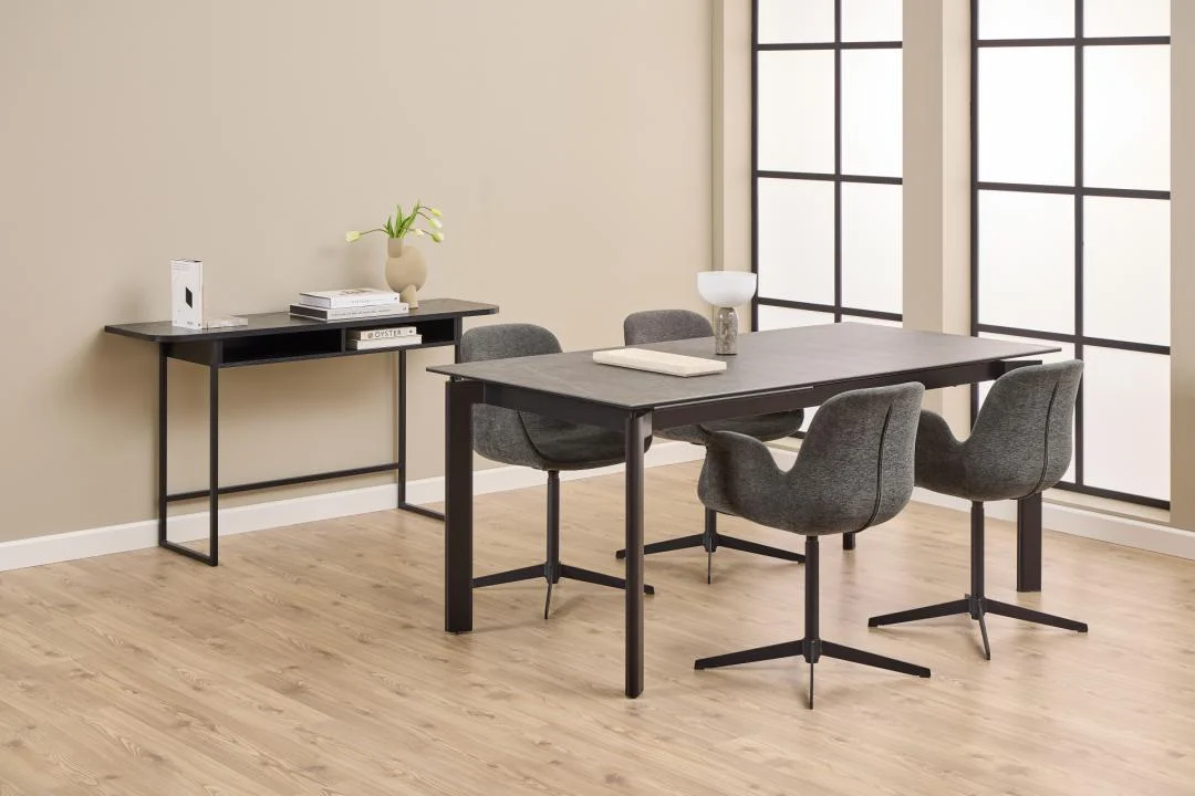 In een eigentijdse eetkamer staat de Eettafel Palermo 90 x 76 CM Rechthoek in zwart keramiek robuust, vier grijs gestoffeerde stoelen, een bijzettafel met bloemen en decor, alles op een licht houten vloer omlijst door grote raampanelen.