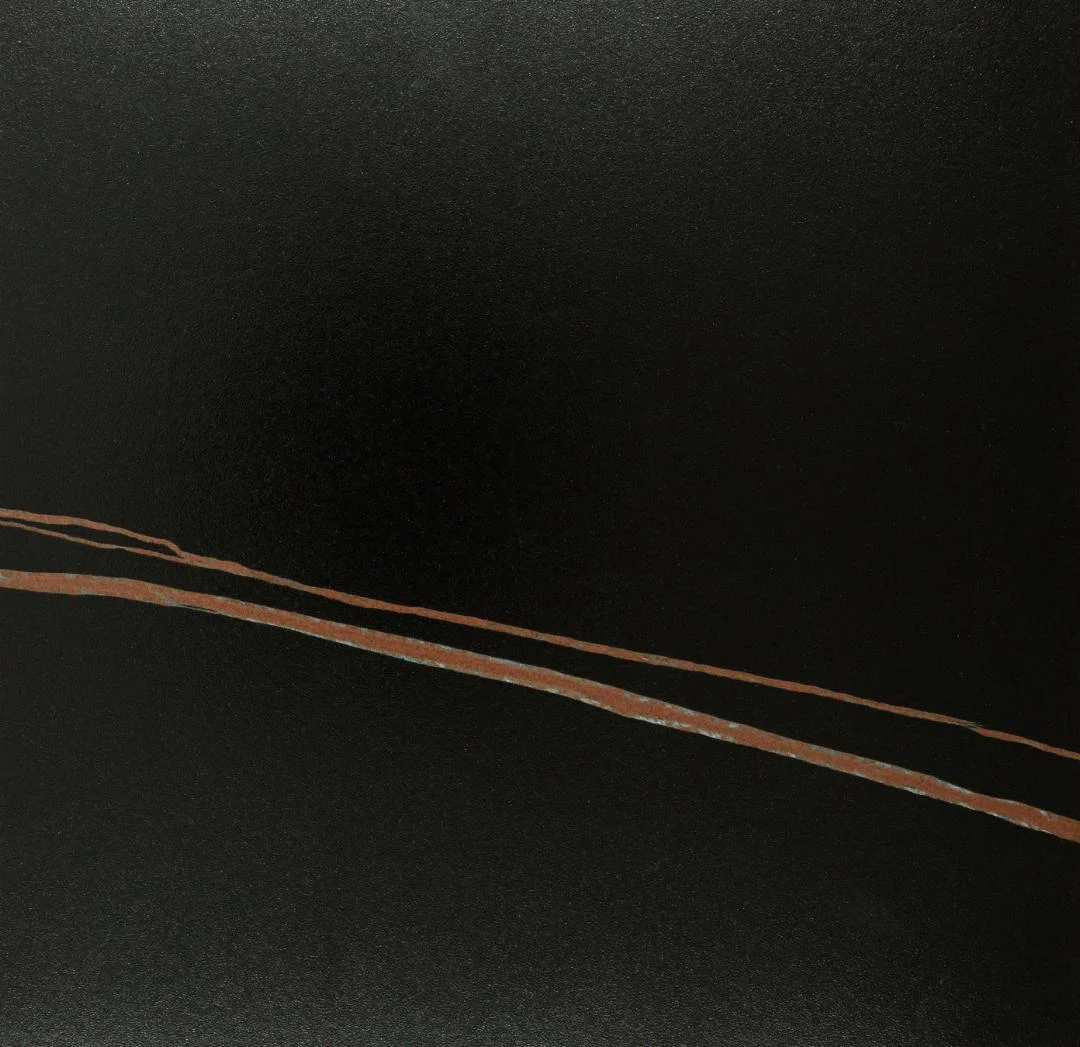 De Eettafel Nieuwe Sfeer (90 x 75 CM, rond) heeft een strak zwart keramiek staal oppervlak dat wordt geaccentueerd door drie parallelle, koperkleurige diagonale lijnen aan de linkeronderkant voor een minimalistisch, modern ontwerp.