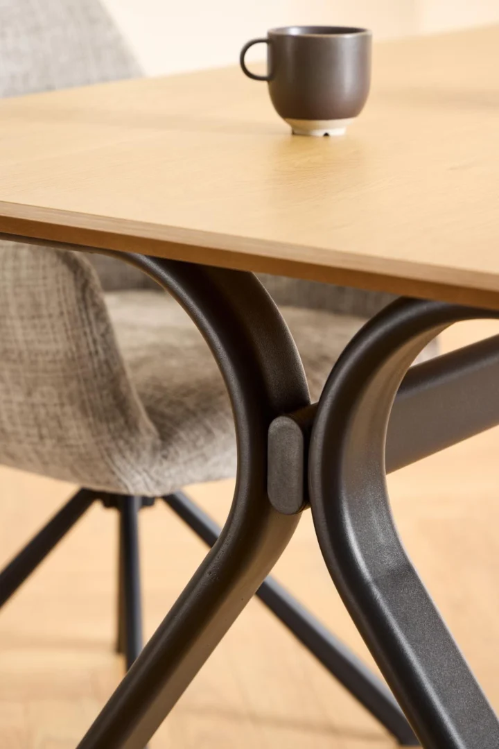 Een close-up van de Eettafel Bristol 100 x 75 CM Rechthoek MDF tafel met zwart metalen poten, een grijs gestoffeerde stoel en een donker keramisch kopje op het tafelblad.