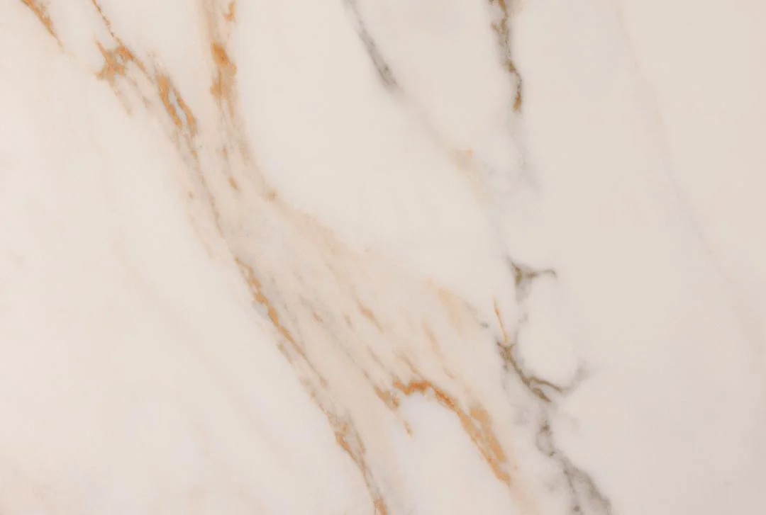 Een close-up van de Eettafel Nieuwe Sfeer 75 CM Rond Keramiek, met lichtgekleurd marmer met subtiele beige, gouden en grijze aderen die diagonaal over het gladde keramische oppervlak lopen.