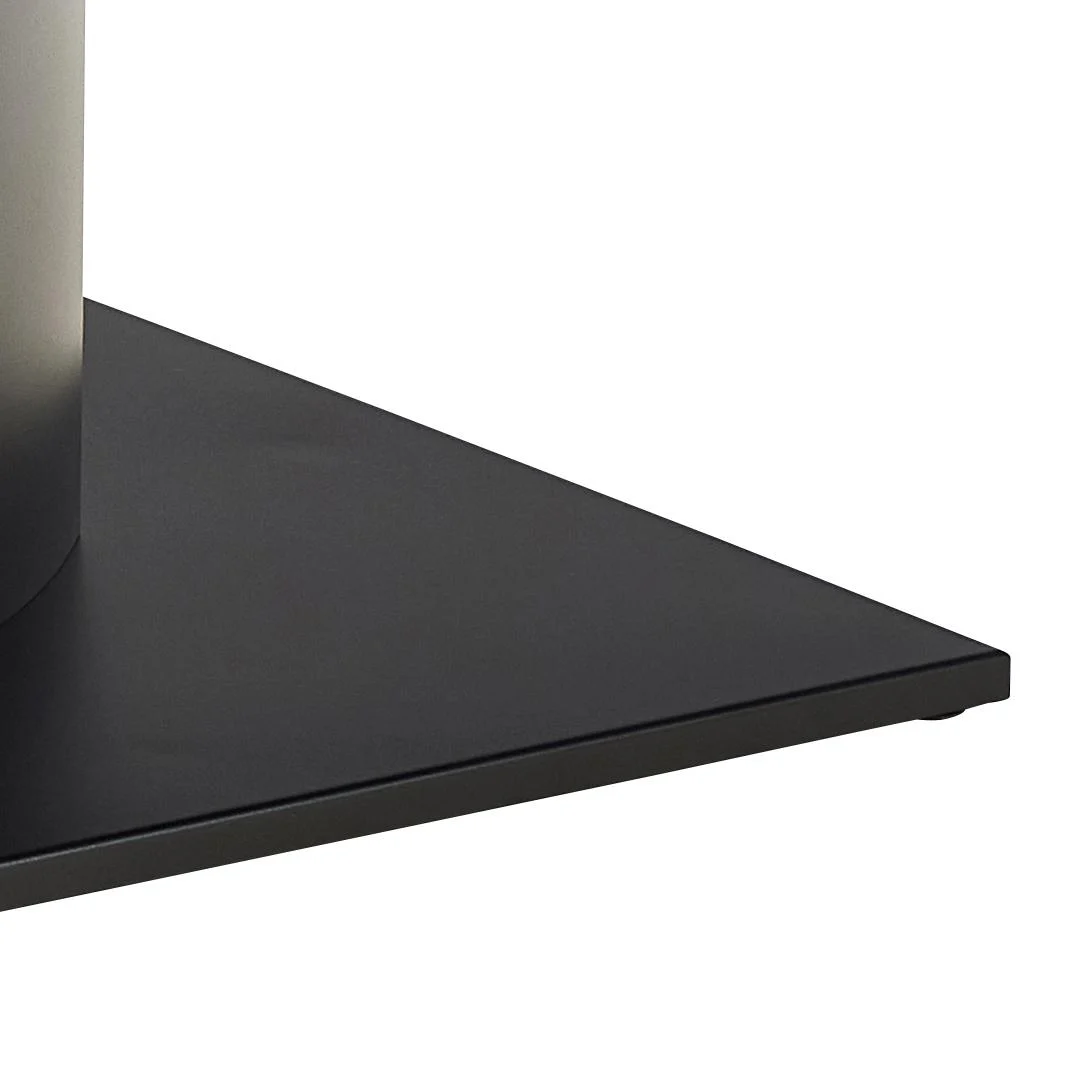 Een close-up van de hoek van de platte, zwart metalen voet van de Eettafel Nieuwe Sfeer 200 x 100 CM Rond, gemaakt van keramiek en metaal, die een cilindrisch metalen object ondersteunt tegen een witte achtergrond.