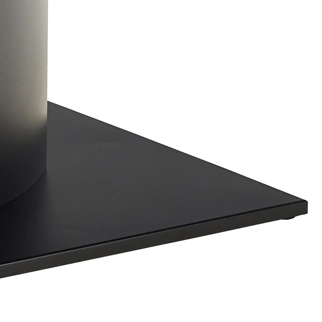 Een close-up van de hoek van de Eettafel Marbella 200 x 100 CM Rechthoek, met een platte, vierkante basis van zwart keramiek en staal die een metalen cilinder ondersteunt, tegen een effen witte achtergrond.