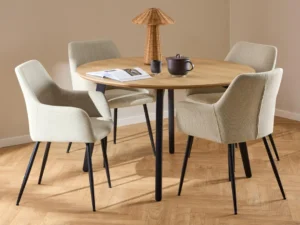 De Eettafel 1 120 CM Rond Eikenhout Staal met een matzwart onderstel wordt omringd door vier lichtbeige gestoffeerde stoelen. Op tafel staan een bruine theepot, een bijpassend kopje, een open boek en een kegelvormige gevlochten lamp.