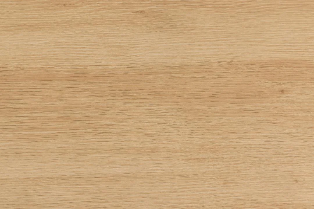 De Eettafel 1 120 CM Rond heeft een lichtbruin eiken tafelblad met een gladde afwerking en subtiele horizontale houtnerf, aangevuld met een mat zwart stalen onderstel.