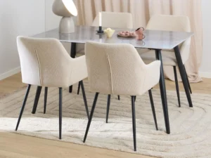 Een moderne eethoek met de Eettafel Nieuwe Sfeer 140 x 80 CM rechthoekige tafel van keramiek en staal, vier beige gestoffeerde stoelen met zwarte poten, een vloerkleed, tafeldecoratie (lamp, kaars, schalen, theepot) en een lichthouten vloer.