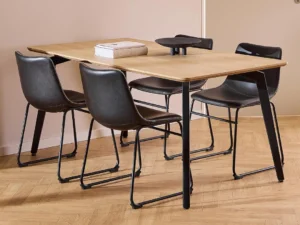 De Eettafel Nieuwe Sfeer (90 x 75 CM, rond) heeft een licht eikenhout oppervlak en zwarte stalen poten, gecombineerd met vier zwartleren stoelen met metalen frames. Op de tafel liggen twee boeken en een zwart decoratief object, op houten vloer.