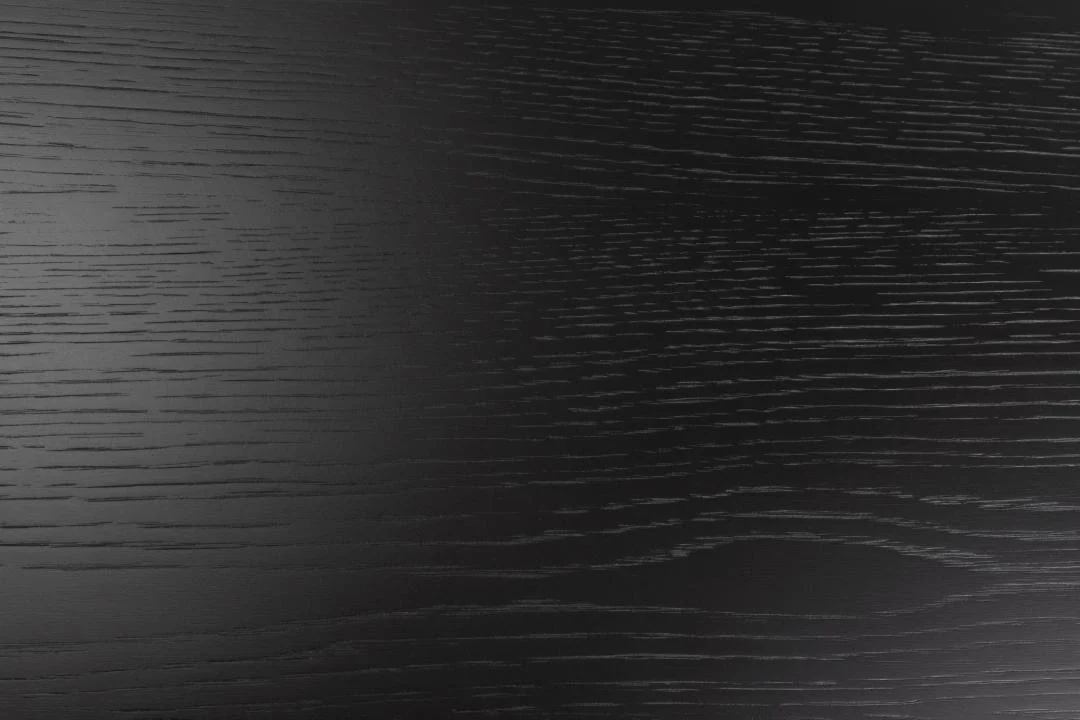 Close-up van de Eettafel Nieuwe Sfeer 115 CM Rond MDF Mat, met de nadruk op het donkere houten oppervlak met subtiele horizontale nerf, gladde matte afwerking, zwarte en grijze tinten en een stevig zwart onderstel.