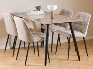 De Eettafel Wicklow 140 x 80 CM Rond heeft een ontwerp van keramiek en staal, gecombineerd met vier beige gestoffeerde stoelen met zwarte poten. Gestyled met gestapelde boeken, een grijze schaal en een witte vaas op een lichthouten vloer tegen een crèmekleurige muur.