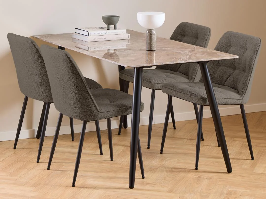 De Eettafel Wicklow 80 x 75 CM Rond Keramiek, gecombineerd met vier grijs gestoffeerde stoelen met zwarte poten, staat op een lichthouten vloer met daarop twee decoratieve schalen en een stapel boeken.