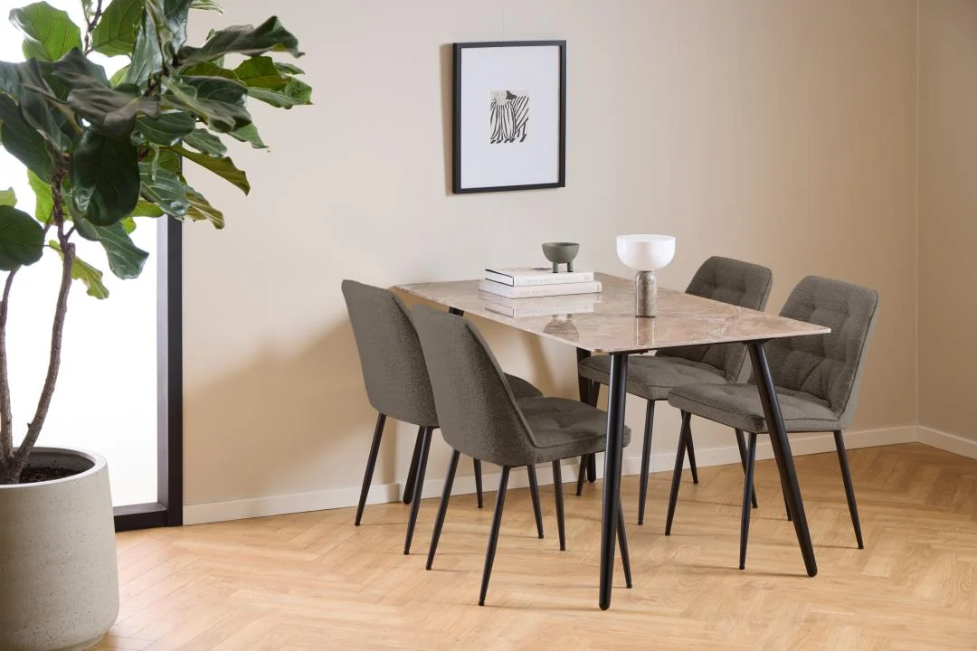 Een moderne eethoek met de Eettafel Wicklow 80 x 75 CM Rond Keramiek, vier grijze stoelen met kussens, boeken, vazen, een grote potplant en ingelijste kunstwerken in een beige kamer met houten visgraatvloeren.