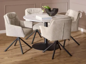 De Eettafel Nieuwe Sfeer 110 CM Rond Marmer Staal, een ronde tafel van wit marmer met een onderstel van zwart staal, is gecombineerd met vier beige gestoffeerde stoelen. Twee boeken en een zwarte vaas met een groene plant staan op de tafel in een kamer met lichthouten vloeren en beige muren.