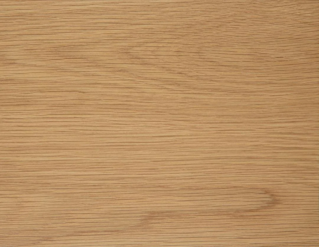 De Eettafel Nieuwe Sfeer 105 CM Rond is gemaakt van eikenhout, met een lichtbruin houten oppervlak met een natuurlijk nerfpatroon dat horizontaal loopt; subtiele kleur- en textuurvariaties en fijne lijnen versterken de ongepolijste, gladde uitstraling.