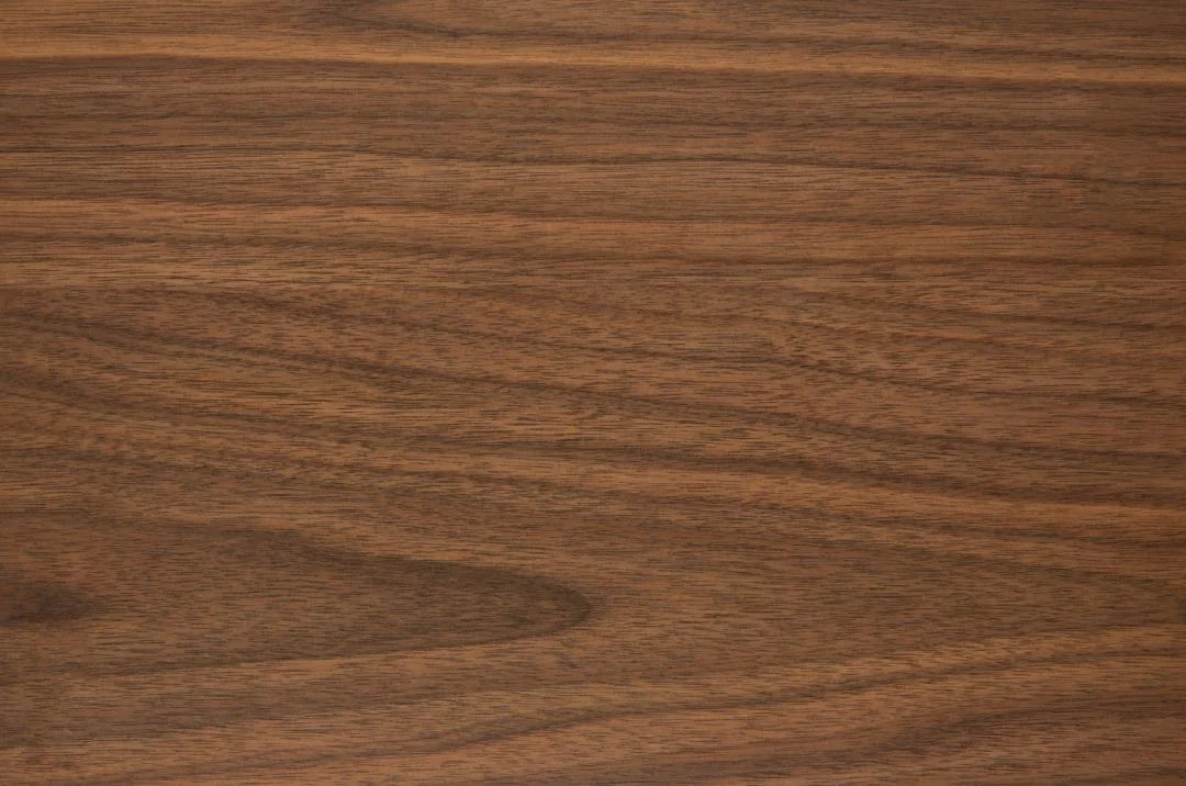 De Eettafel Roxby 105 CM Rond Notenhout heeft een glad, rond houten oppervlak met een rijke bruine kleur en natuurlijke horizontale nerfpatronen.