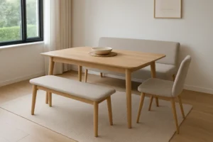 Een minimalistische eethoek met een lichte houten tafel, een bank, een stoel met kussens en een kleine sofa op een beige vloerkleed in de buurt van dunne gordijnen. In tegenstelling tot een salontafel of bijzettafel is deze opstelling meer gericht op dineren dan op loungen.