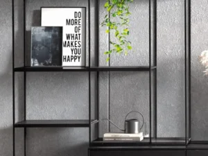 De Izola BOEKENREK DO, een strakke zwarte metalen plank, staat tegen een grijze muur met ingelijste kunst (op een ervan staat "DO MORE OF WHAT MAKES YOU HAPPY"), een hangende plant, gieter en decoratieve vazen.