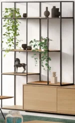 De Izola BOEKENREK E02M is een moderne stellingkast met een zwart metalen frame en houten planken, ideaal voor het uitstallen van potplanten, keramische vazen, een kleine paardensculptuur en minimalistische decoratie tegen een lichte muur.