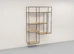 De Izola BOEKENREK HANG E02M is een moderne, minimalistische wandkast met een zwart metalen frame en licht houten planken in een asymmetrisch geometrisch ontwerp tegen een witte muur.