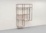 De Izola BOEKENREK HANG WWM is een modern, geometrisch wandrek met een zwart metalen frame en licht houten planken, met een asymmetrisch open doosontwerp voor stijlvolle opbergruimte.