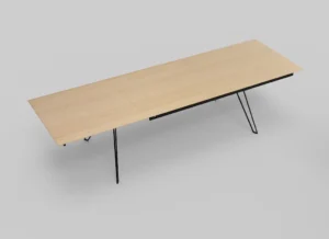 De Izola TAFEL 220-320 E02M is een grote, rechthoekige houten tafel met een licht blad en slanke zwarte metalen poten, tegen een effen grijze achtergrond.