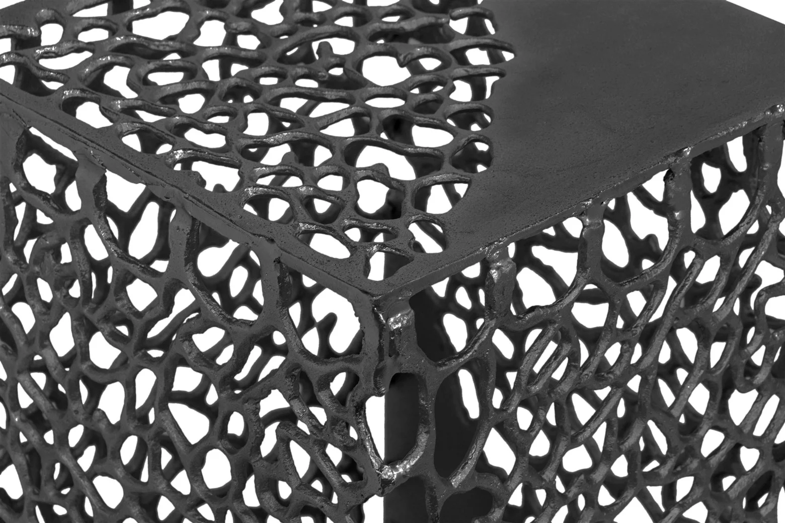 Close-up van de Bijzettafel Zwart Aluminium Set met een zwart metalen kubus met een open, web-achtig patroon en een gladde massieve hoek aan de bovenkant, waardoor het licht door het ingewikkelde ontwerp filtert.