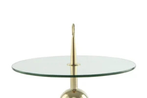 De Bijzettafel Transparant, Goud Staal is een moderne ronde glazen tafel met een centrale goudstalen steun met daarop een puntige punt en een ronde lus. Het metalen onderstel is gedeeltelijk zichtbaar.