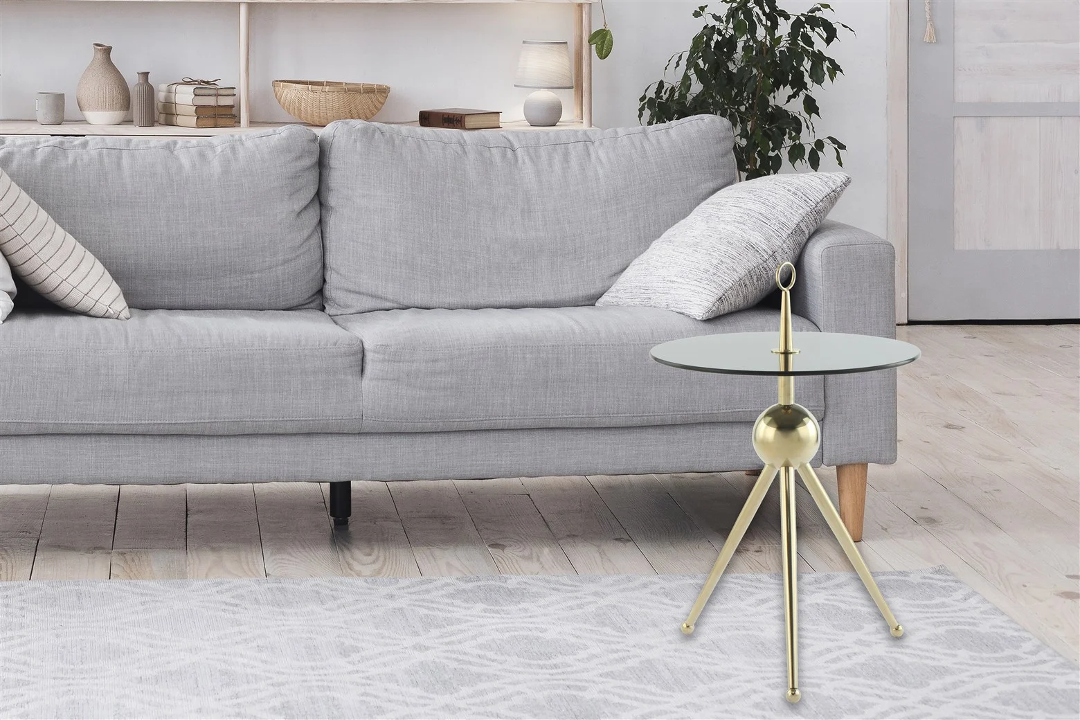 Een moderne woonkamer met een lichtgrijze bank, witte en gedessineerde kussens, een Bijzettafel Grijs, Goud Staal rond bijzettafeltje, een gedessineerd grijs vloerkleed, een plant en minimaal houten decor op planken op de achtergrond.