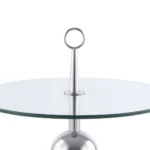 De Bijzettafel Transparant, Zilver Staal is een moderne ronde glazen tafel met een zilver metalen onderstel, voorzien van een centrale paal met een ronde handgreep.