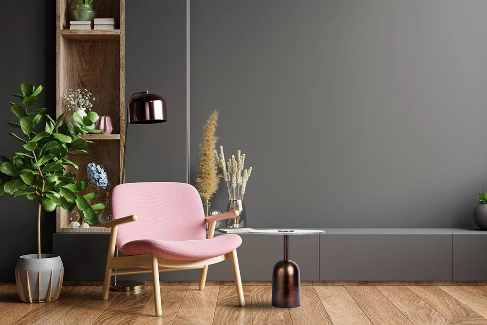 Een moderne woonkamer met een roze stoel, planten in potten, decoratief gras, een houten kast, houten vloer en een Bijzettafel Groen Marmer als klein rond bijzettafeltje tegen een grijze muur.