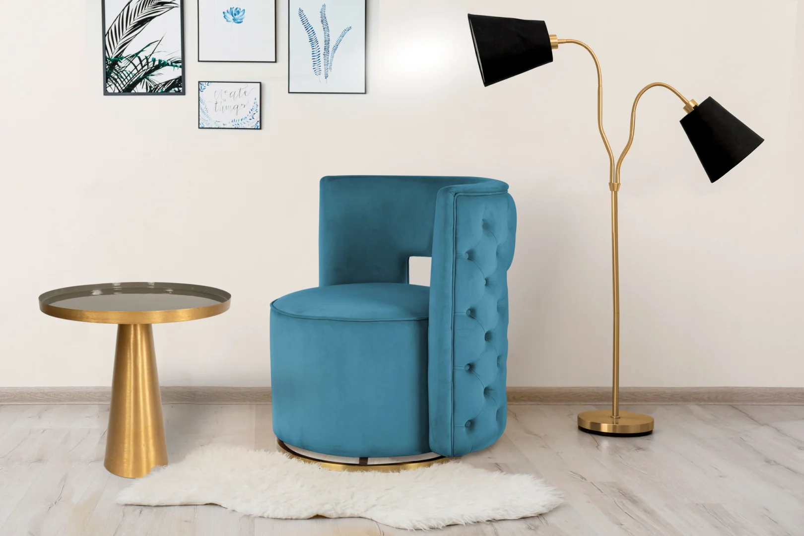 Een moderne kamer is voorzien van de Bijzettafel Grijs Ijzer, een blauw fluwelen getufte stoel, een hoge gouden vloerlamp met zwarte kappen, een wit vloerkleed en ingelijste kunst op een crèmekleurige muur.