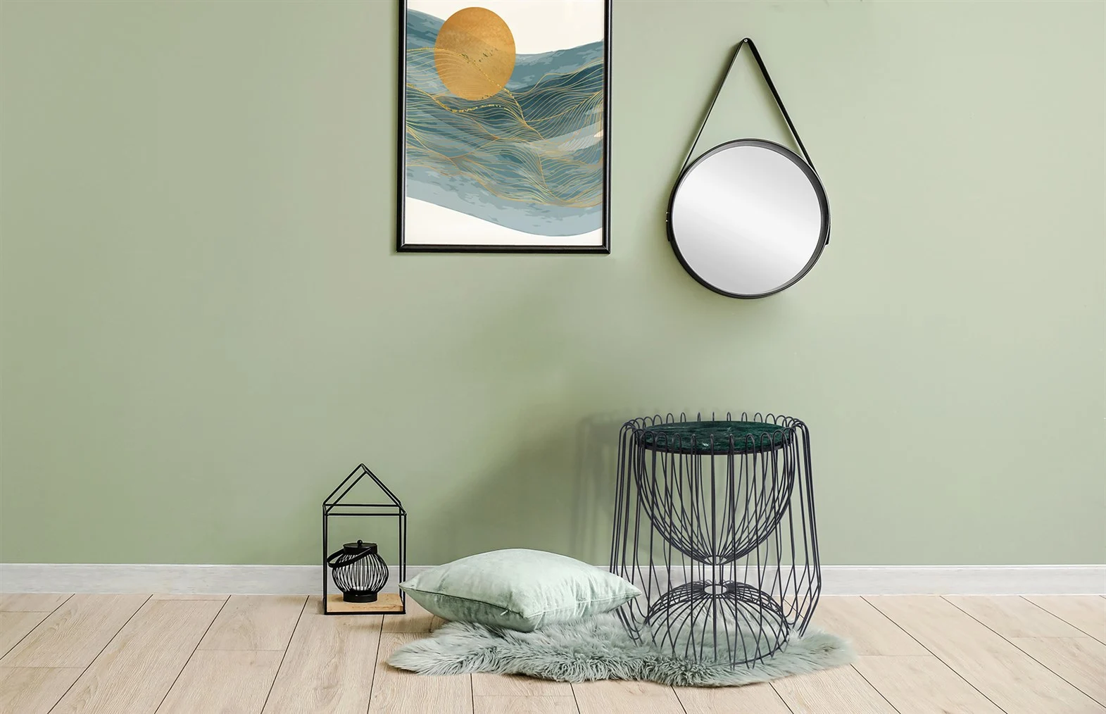 Minimalistische kamer met lichtgroene muur, houten vloer, abstracte kunst, ronde spiegel, Bijzettafel Zwart, Groen Rond Marmer als bijzettafel, lantaarn met kaars, groen vloerkussen en donzig groen vloerkleed.