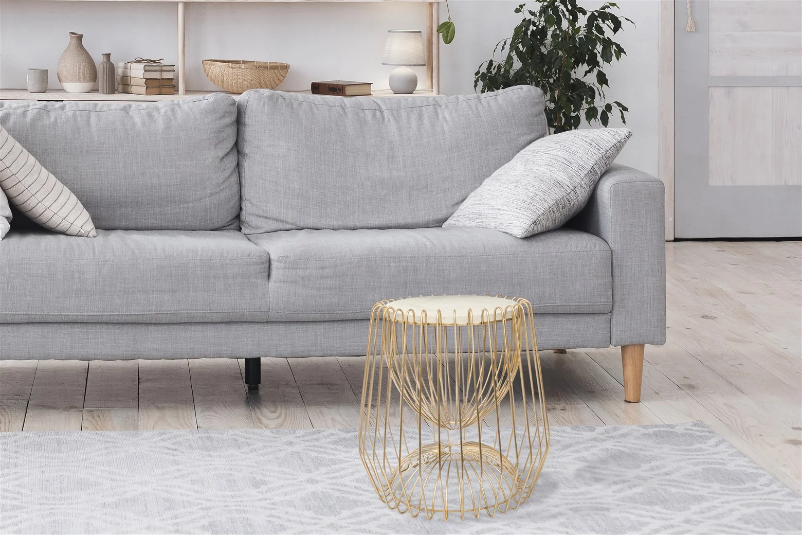 Een moderne woonkamer met een lichtgrijze bank, gedessineerde kussens, de Bijzettafel Messing, Wit Rond Marmer bijzettafel, een gedessineerd vloerkleed, kamerplanten en lichte houten vloeren in een lichte, luchtige ruimte.