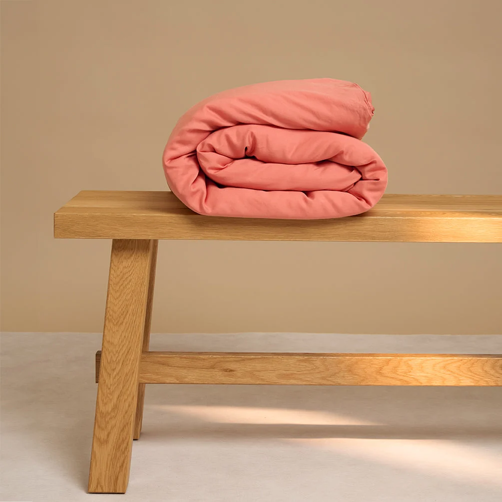 De Dekbedovertrek 100x135 voor de slaapkamer is netjes opgerold en geplaatst op een eenvoudige houten bank tegen een beige achtergrond.