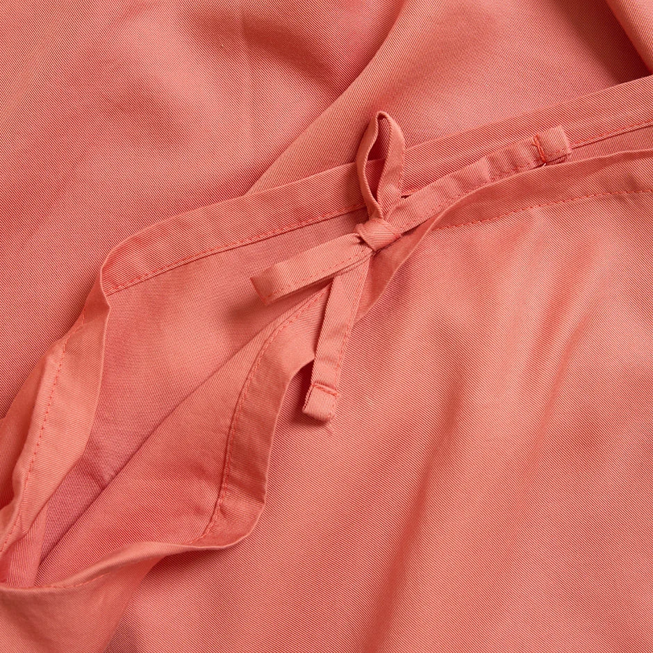 Een close-up van de Dekbedovertrek 100x135 voor de slaapkamer toont gladde roze stof, een gevouwen naad en een klein strikje gemaakt van stroken stof met zichtbaar stiksel langs de rand.