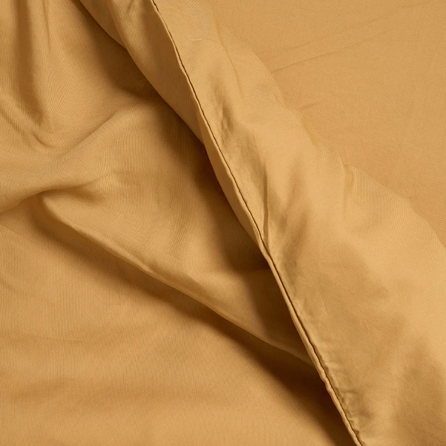 Een close-up van de Dekbedovertrek Geel 100x135 voor de slaapkamer toont de mosterdgele stof met een zachte textuur en een zichtbare gevouwen rand, perfect om warmte toe te voegen aan je slaapkamer.