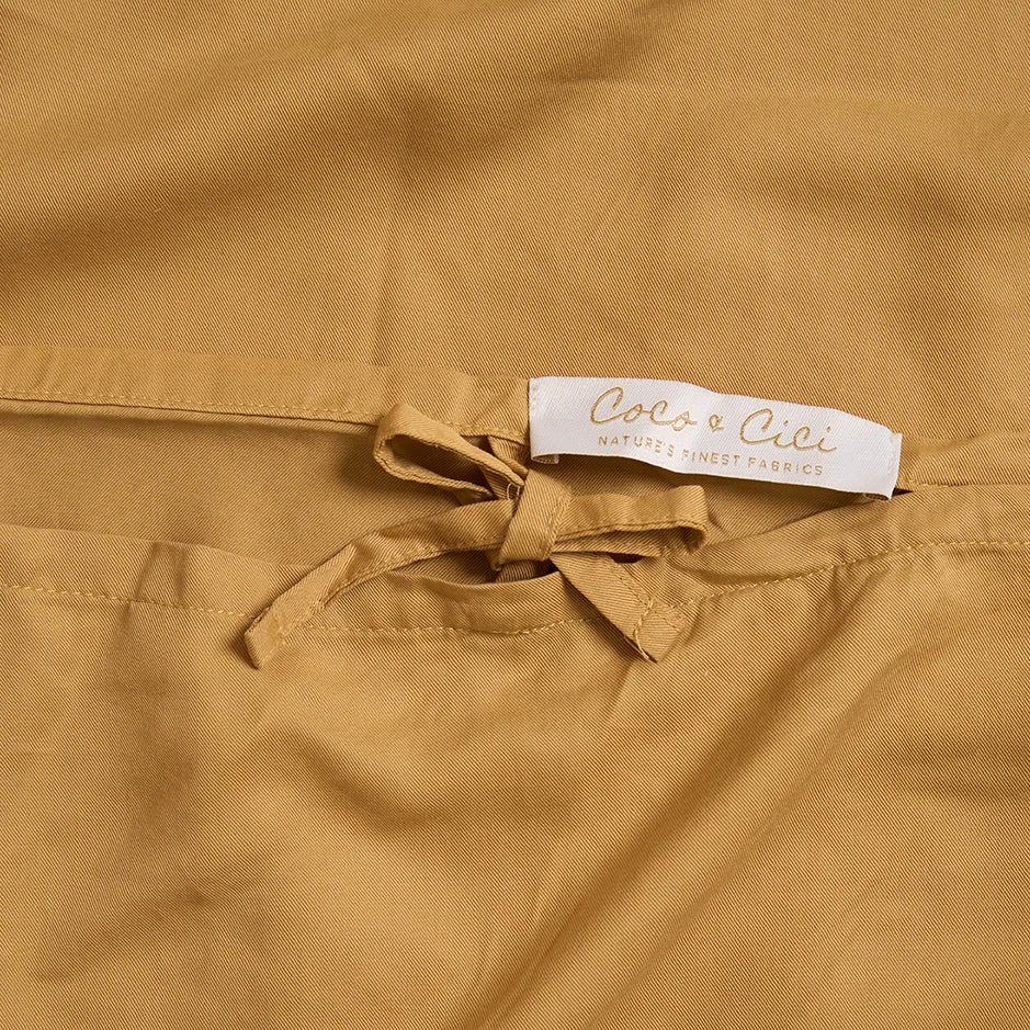 Een close-up van een bruine stof Dekbedovertrek Geel 100x135 voor de slaapkamer met een klein strikje en een wit label met de tekst Coco e Cici Natures Finest Fabrics.