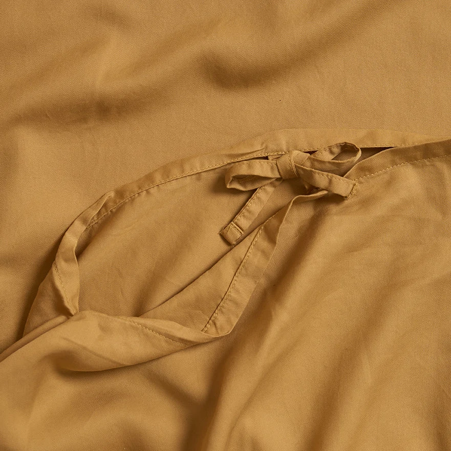 Close-up van de Dekbedovertrek Geel 100x135 voor de slaapkamer: lichtbruine stof met een klein, gedeeltelijk geknoopt bandje bovenop, met een zachte, gladde textuur en zachte plooien.