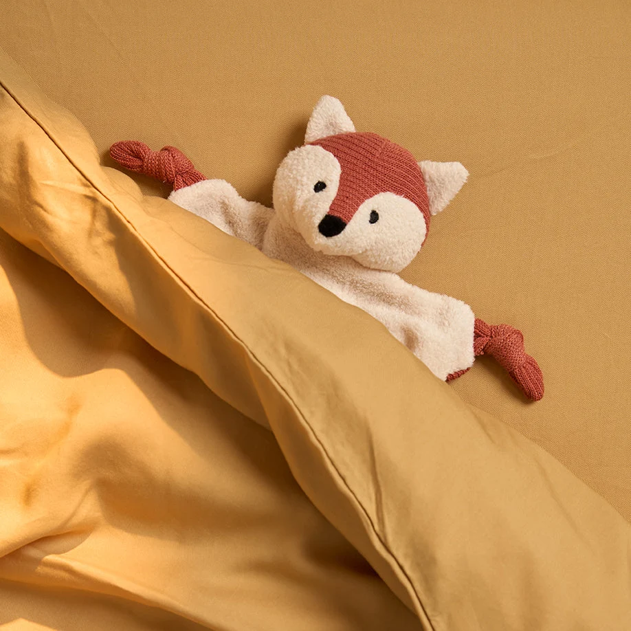 Een pluche speelgoedvos gluurt onder de Dekbedovertrek 120x150 Geel voor elk seizoen vandaan, met zijn rood-witte lijf knus onder de mosterdgele lakens.