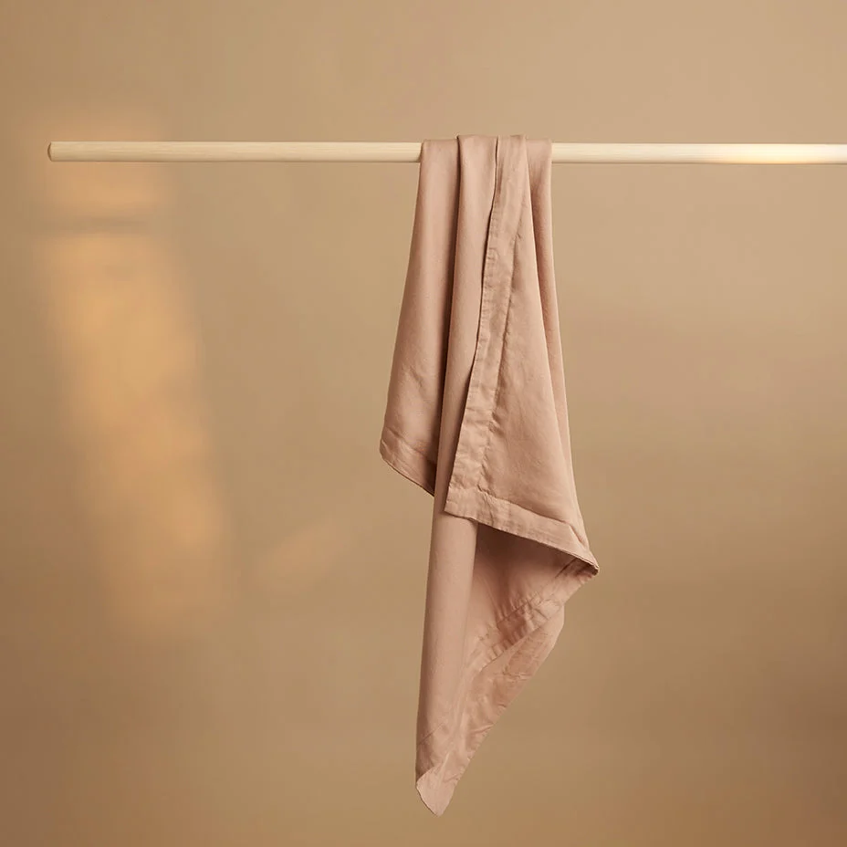 Studiofoto van een perzik kleurige kussensloop van TENCEL Lyocell, hangend aan een houten stok. Zachte, egale belichting.