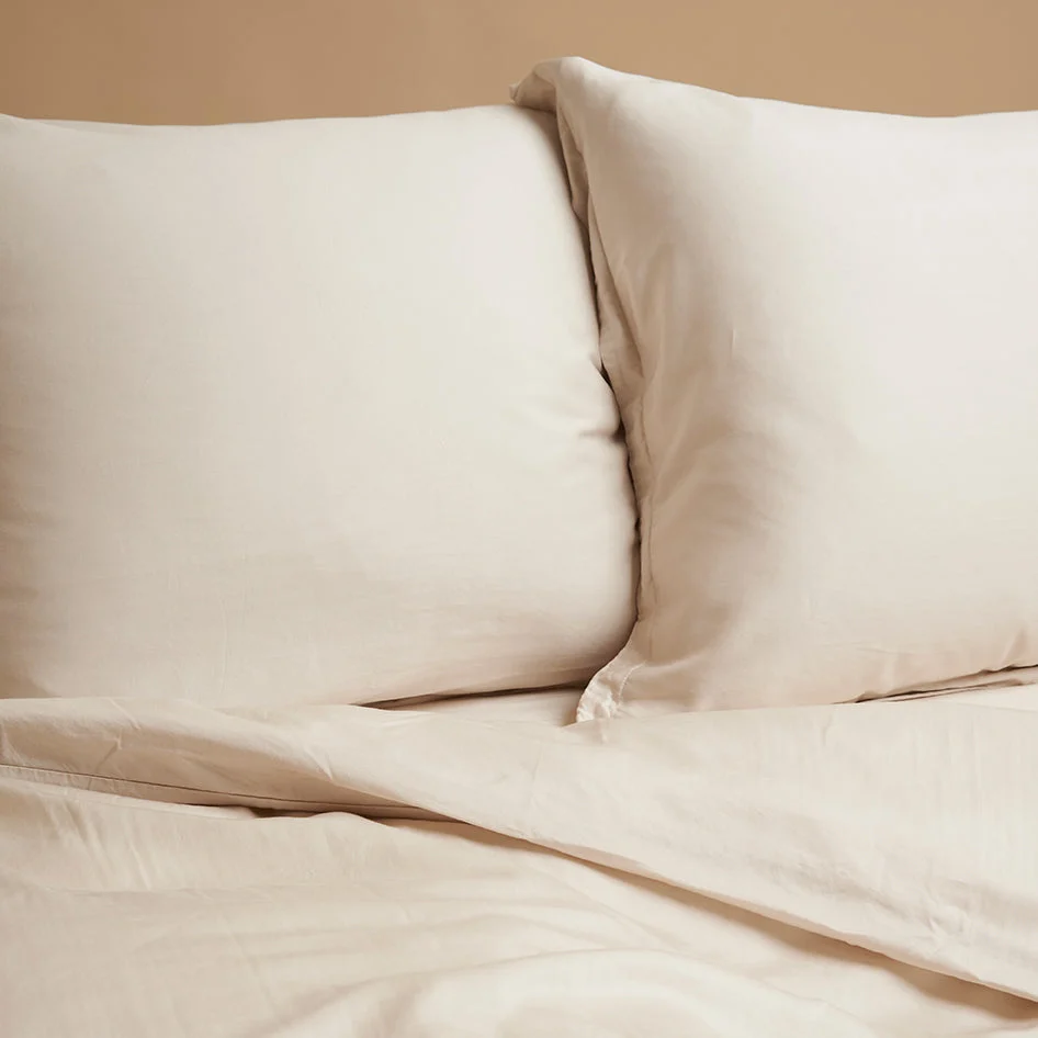 Beige kussensloop van TENCEL Lyocell, formaat 60x70 cm. Zachte stof in warme tint, subtiele plooien. Close-up, natuurlijk licht.