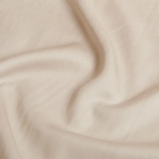 Close-up van een beige ledikant hoeslaken, zachte plooien. TENCEL™ Twill stof met subtiele glans, natuurlijk licht.