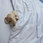 Lichtblauw hoeslaken met gebreide olifant. Zachte tinten, gladde textuur. Boven aanzicht, zacht licht. Ideaal voor babykamer decoratie.